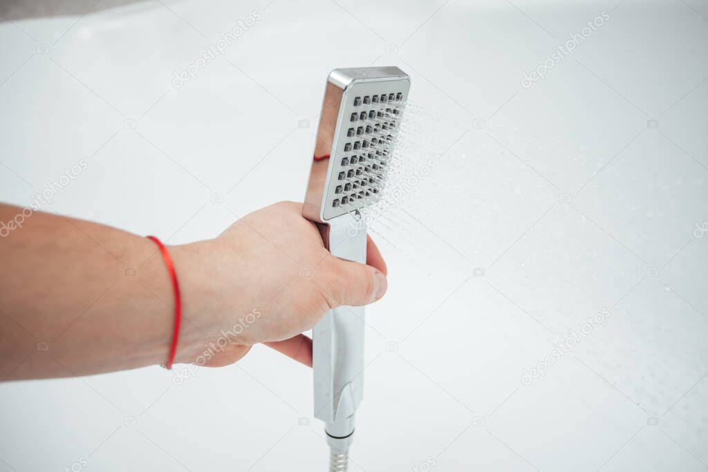 Male hand holding shower against white wall in bathroom, closeup shot 