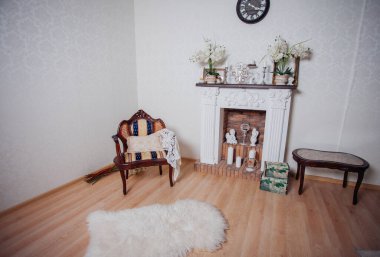 Studio interior. Living room with fireplace and soft armchair and ottoman. Bright interior of cozy lounge. Glossy wooden parquet floor