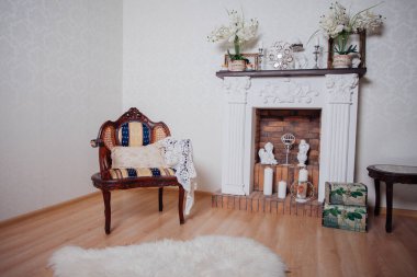 Studio interior. Living room with fireplace and soft armchair and ottoman. Bright interior of cozy lounge. Glossy wooden parquet floor