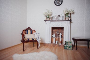 Studio interior. Living room with fireplace and soft armchair and ottoman. Bright interior of cozy lounge. Glossy wooden parquet floor