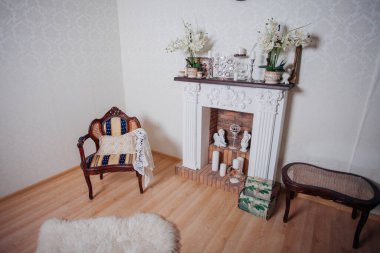 Studio interior. Living room with fireplace and soft armchair and ottoman. Bright interior of cozy lounge. Glossy wooden parquet floor