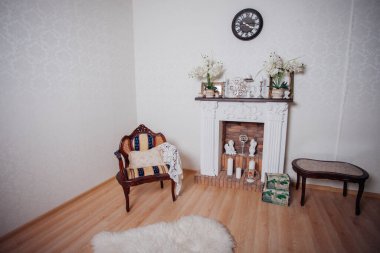 Studio interior. Living room with fireplace and soft armchair and ottoman. Bright interior of cozy lounge. Glossy wooden parquet floor