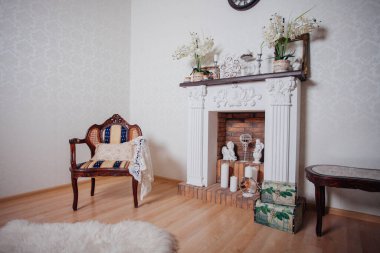 Studio interior. Living room with fireplace and soft armchair and ottoman. Bright interior of cozy lounge. Glossy wooden parquet floor