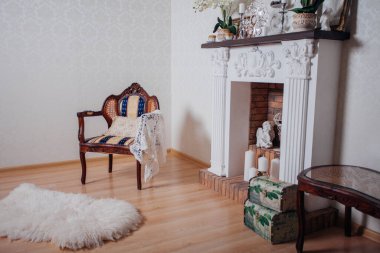 Studio interior. Living room with fireplace and soft armchair and ottoman. Bright interior of cozy lounge. Glossy wooden parquet floor