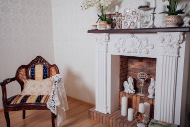 Studio interior. Living room with fireplace and soft armchair and ottoman. Bright interior of cozy lounge. Glossy wooden parquet floor