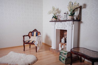 Studio interior. Living room with fireplace and soft armchair and ottoman. Bright interior of cozy lounge. Glossy wooden parquet floor