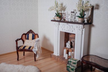 Studio interior. Living room with fireplace and soft armchair and ottoman. Bright interior of cozy lounge. Glossy wooden parquet floor