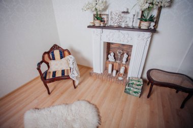 Studio interior. Living room with fireplace and soft armchair and ottoman. Bright interior of cozy lounge. Glossy wooden parquet floor