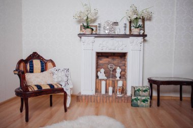 Studio interior. Living room with fireplace and soft armchair and ottoman. Bright interior of cozy lounge. Glossy wooden parquet floor