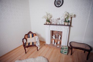 Studio interior. Living room with fireplace and soft armchair and ottoman. Bright interior of cozy lounge. Glossy wooden parquet floor