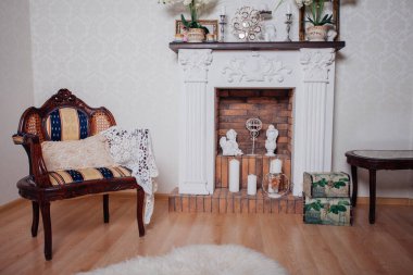 Studio interior. Living room with fireplace and soft armchair and ottoman. Bright interior of cozy lounge. Glossy wooden parquet floor