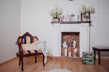 Studio interior. Living room with fireplace and soft armchair and ottoman. Bright interior of cozy lounge. Glossy wooden parquet floor