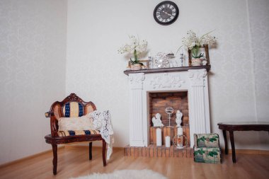 Studio interior. Living room with fireplace and soft armchair and ottoman. Bright interior of cozy lounge. Glossy wooden parquet floor