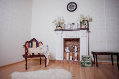 Studio interior. Living room with fireplace and soft armchair and ottoman. Bright interior of cozy lounge. Glossy wooden parquet floor
