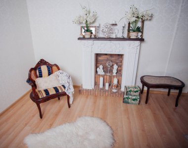 Studio interior. Living room with fireplace and soft armchair and ottoman. Bright interior of cozy lounge. Glossy wooden parquet floor