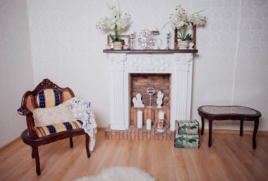 Studio interior. Living room with fireplace and soft armchair and ottoman. Bright interior of cozy lounge. Glossy wooden parquet floor