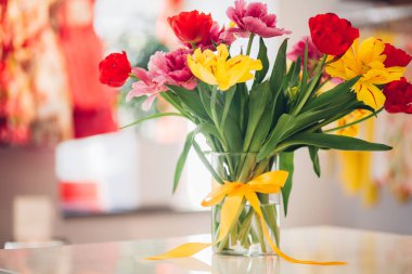 Vazoda düğümlenmiş fiyonk, suda çiçekler, farklı renklerde laleler, ev dekorasyonu.