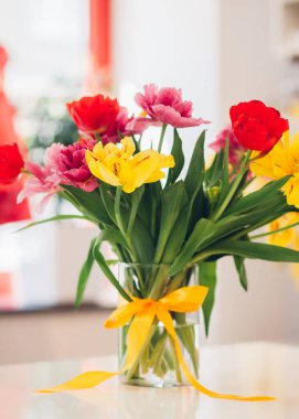 Vazoda düğümlenmiş fiyonk, suda çiçekler, farklı renklerde laleler, ev dekorasyonu.