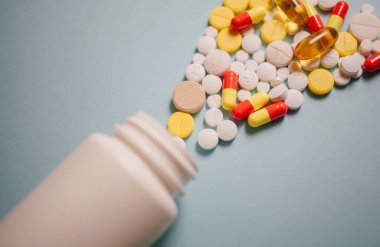 Çeşitli ilaç hapları, haplar, kapsüller ve mavi arka planda şişe.