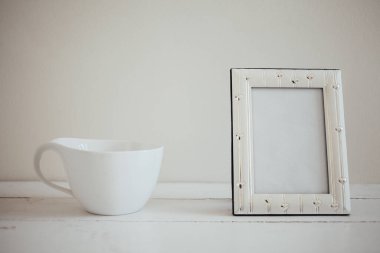 Fotoğraf çerçevesi ve kahve fincanı ahşap masadaki masa örtüsünün üzerinde.