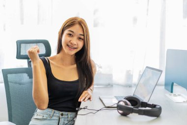 Kazanan! Hoş, sevimli, neşeli, neşeli, mutlu Asyalı kızın portresi üniversitede kutlayan dizüstü bilgisayarla koltukta oturuyor, bir elini kaldırıyor ve kazanıyor.