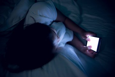 Geceleri yatakta akıllı telefondan oyun oynayan Asyalı kadın.