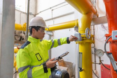 Kazan dairesinde çalışan gözlüklü Asyalı mühendis ısıtma sistemi ekipmanlarının teknik verilerini kontrol ediyor.