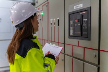 Asyalı elektrik mühendisi kontrol odasındaki elektrik sistemini kontrol etmek ve izlemek için pano tutuyor.,