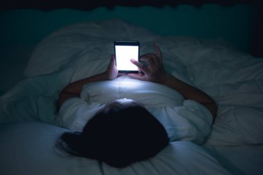 Geceleri yatakta akıllı telefondan oyun oynayan Asyalı kadın.