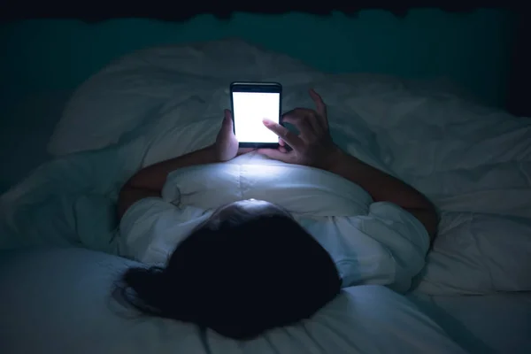 Asian woman playing game on smartphone in the bed at nighttime