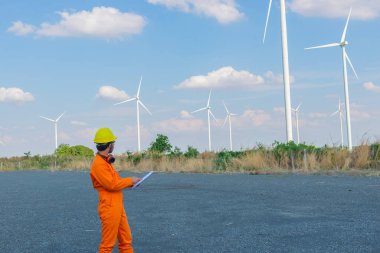 İnsan mühendisinin silueti rüzgar türbini çiftliği güç jeneratörü istasyonunda çalışıyor ve raporu tutuyor.