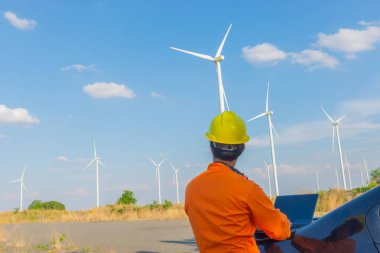İnsan mühendisinin silueti rüzgar türbini çiftliği güç jeneratörü istasyonunda çalışıyor ve raporu tutuyor.