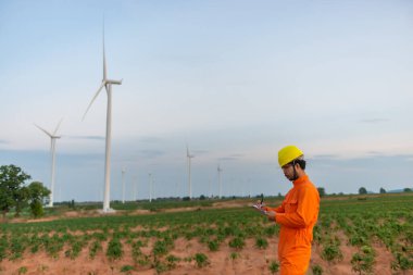 İnsan mühendisinin silueti rüzgar türbini çiftliği güç jeneratörü istasyonunda çalışıyor ve raporu tutuyor.