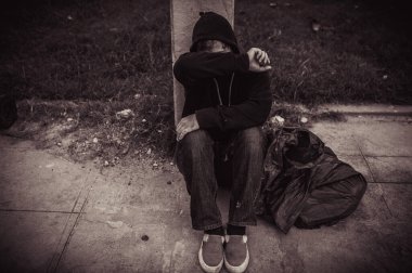 Asyalı evsiz adam yol kenarında oturuyor.