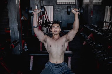 Spor salonunda çalışan yakışıklı bir adam, ağırlık kaldıran Asyalı bir adam spor müsabakası için ağırlık kaldıran, omuz kaslarını çalıştırmak için dambılları iten bir adam..