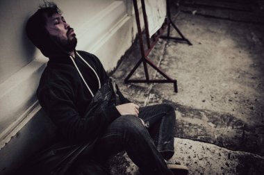 Asyalı evsiz adam yol kenarında oturuyor.