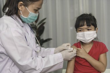 Tıbbi maske takan bir kıza virüsü korumak için aşı yapan Asyalı doktor.