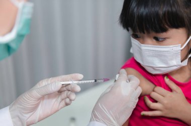 Tıbbi maske takan bir kıza virüsü korumak için aşı yapan Asyalı doktor.