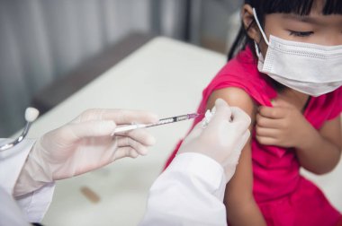 Tıbbi maske takan bir kıza virüsü korumak için aşı yapan Asyalı doktor.