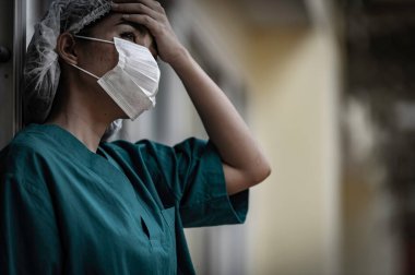 Depresyonda olan Asyalı kadın hemşire hastane zemininde otururken maske takıyor.