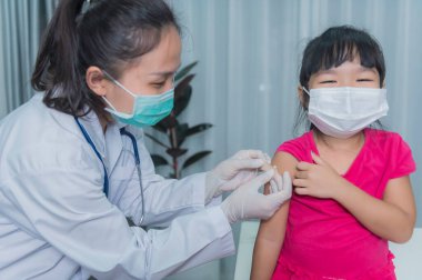Tıbbi maske takan bir kıza virüsü korumak için aşı yapan Asyalı doktor.