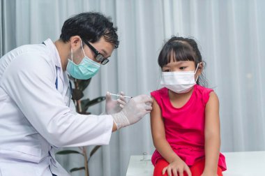 Tıbbi maske takan bir kıza virüsü korumak için aşı yapan Asyalı doktor.