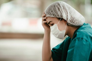 Depresyonda olan Asyalı kadın hemşire hastane zemininde otururken maske takıyor.