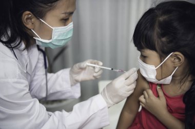 Tıbbi maske takan bir kıza virüsü korumak için aşı yapan Asyalı doktor.