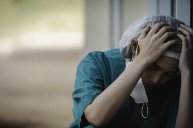 Depresyonda olan Asyalı kadın hemşire hastane zemininde otururken maske takıyor.