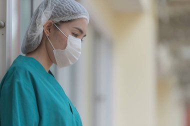 Depresyonda olan Asyalı kadın hemşire hastane zemininde otururken maske takıyor.