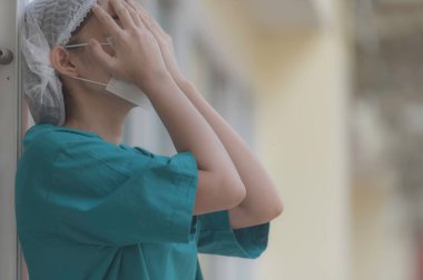 Depresyonda olan Asyalı kadın hemşire hastane zemininde otururken maske takıyor.