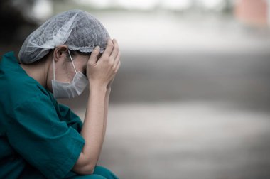 Depresyonda olan Asyalı kadın hemşire hastane zemininde otururken maske takıyor.