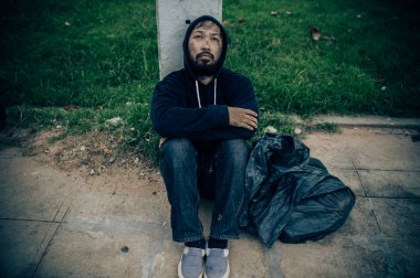 Asyalı evsiz adam yol kenarında oturuyor.