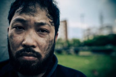 Asyalı evsiz adam yol kenarında oturuyor.